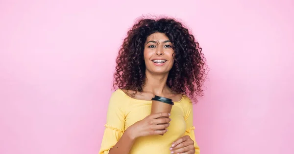 Curly young woman holding coffee to go isolated on pink — Stock Photo