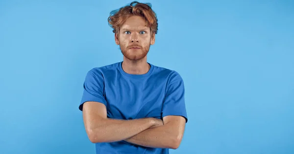 Bearded and redhead man in t-shirt standing with crossed arms isolated on blue — Stock Photo