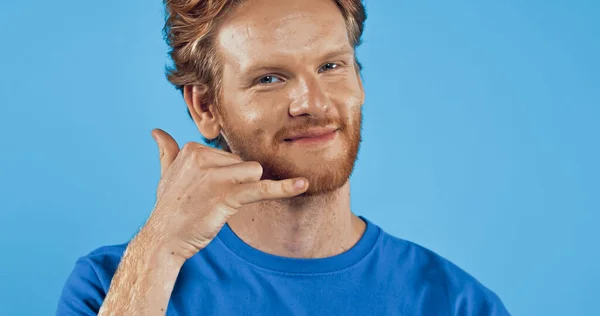 Barbudo y pelirrojo hombre en camiseta mostrando llámame gesto aislado en azul - foto de stock