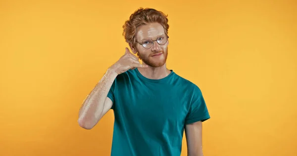 Pelirrojo hombre en camiseta mostrando llámame gesto aislado en amarillo - foto de stock