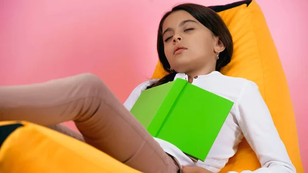 Niño durmiendo con libro en bolsa de frijol silla en rosa - foto de stock