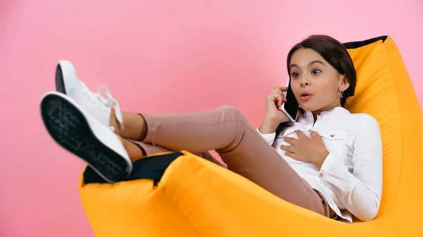 Criança pré-adolescente falando no smartphone e descansando na cadeira de saco de feijão em rosa — Fotografia de Stock