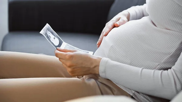 Vista cortada da mulher grávida tocando barriga enquanto segurando ultra-som — Fotografia de Stock