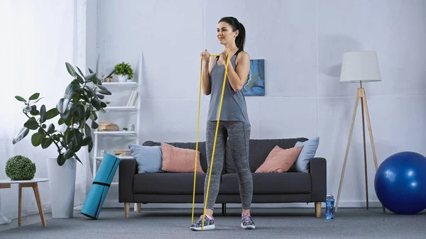 Feliz joven en ropa deportiva trabajando con elásticos en casa - foto de stock