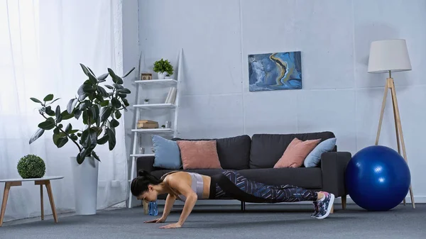 Jeune femme en vêtements de sport faire de l'exercice de planche à la maison — Photo de stock