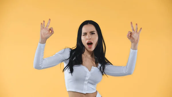 Excited woman showing okay signs while winking at camera isolated on yellow — Stock Photo