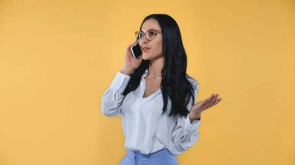 Smiling businesswoman gesturing while talking on mobile phone isolated on yellow — Stock Photo