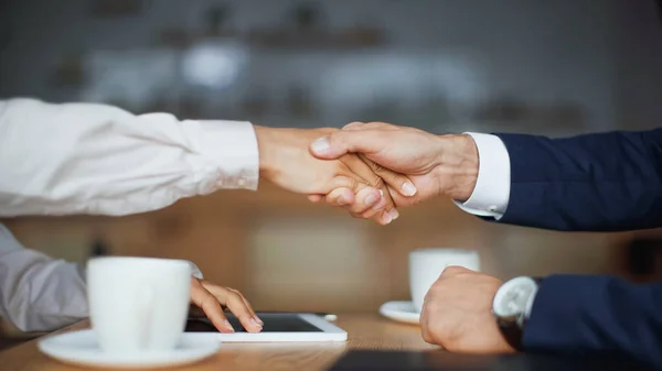 Cropped view of businesswoman and businessman shaking hands in cafe — Stock Photo