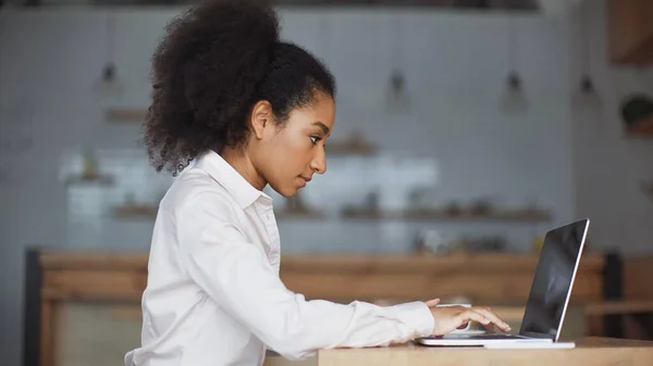 Vista lateral de la mujer afroamericana usando el ordenador portátil en la cafetería - foto de stock