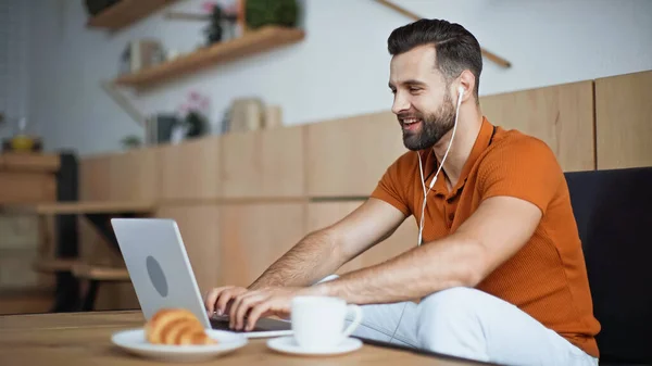 Cheerful man listening music in earphones and using laptop in cafe — Stock Photo