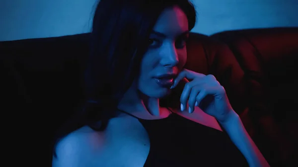 Red lighting on face of seductive brunette woman on blue — Stock Photo