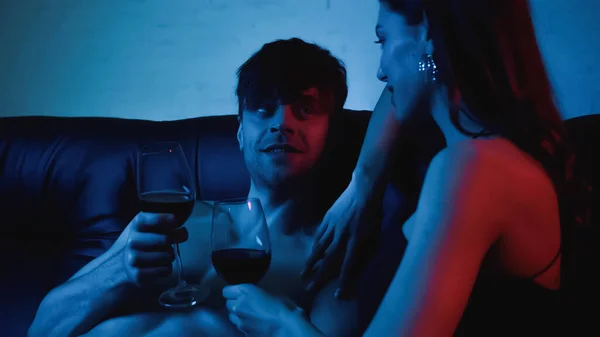 Uomo senza maglietta e fidanzata sexy che tiene bicchieri di vino su blu — Foto stock