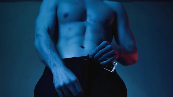 Частичный вид сексуального и мускулистого мужчины раздевающегося на голубом — стоковое фото