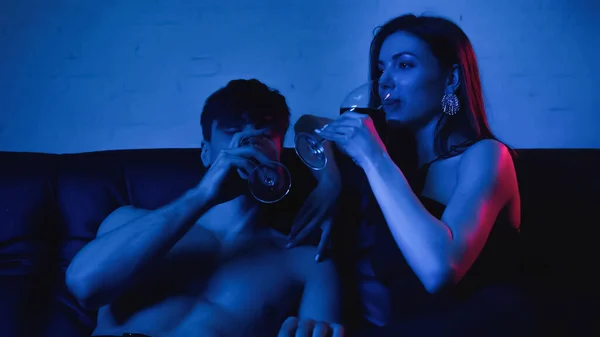 Casal sexy segurando óculos enquanto bebe vinho em azul — Fotografia de Stock