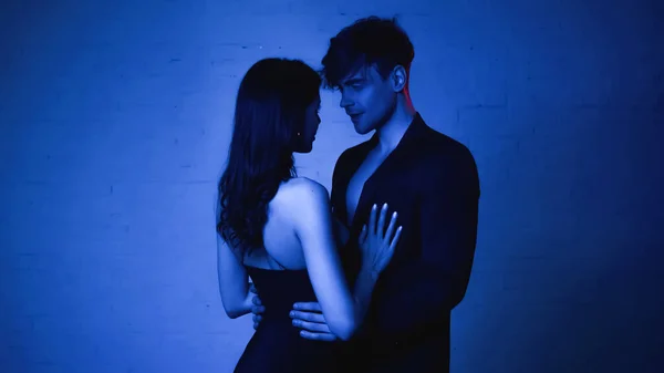 Femme séduisante en robe embrassant l'homme en blazer sur bleu — Photo de stock