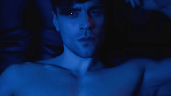 Iluminación azul en el hombre sin camisa mirando a la cámara - foto de stock