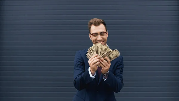 Glücklicher Geschäftsmann im Anzug lächelt, während er Dollars hält — Stockfoto