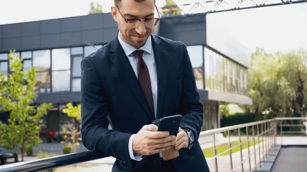 Homem de negócios feliz em óculos e terno usando smartphone — Fotografia de Stock