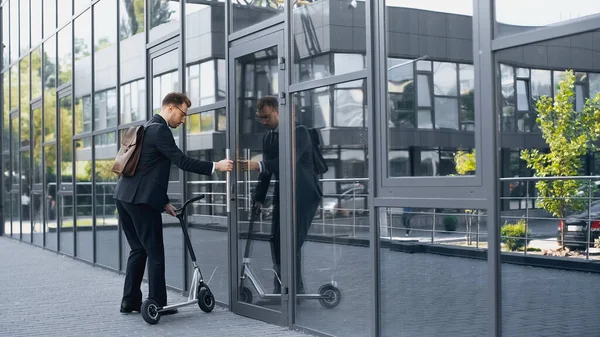 Hombre de negocios con traje y mochila caminando en el edificio con scooter eléctrico - foto de stock