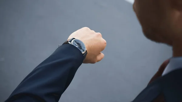 Recortado vista de hombre de negocios en desgaste formal mirando reloj de pulsera mientras espera fuera - foto de stock