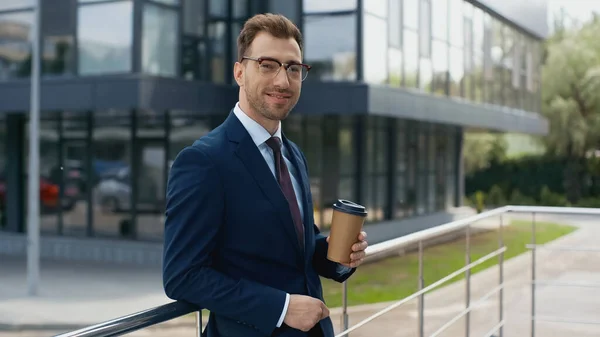 Homem de negócios sorridente em desgaste formal segurando café para sair — Fotografia de Stock