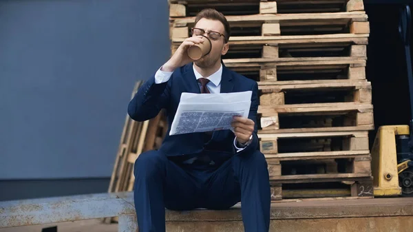 Empresário sentado enquanto bebe café para ir e ler jornal fora — Fotografia de Stock
