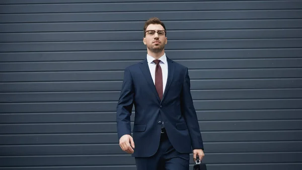 Confident businessman in suit walking with briefcase near building — Stock Photo