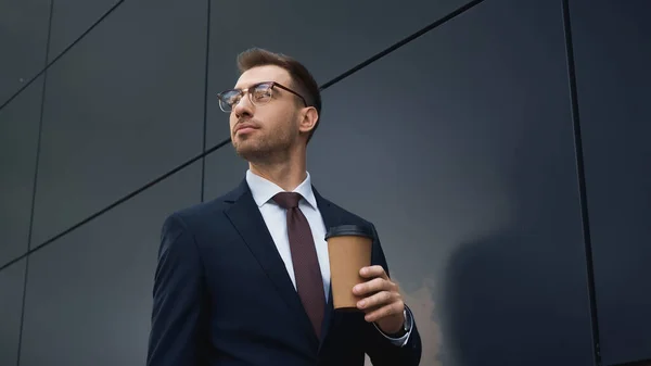 Businessman in formal wear holding coffee to go and looking away outside — Stock Photo