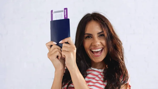 Mujer excitada sosteniendo pasaporte con billete de avión y mirando a la cámara - foto de stock