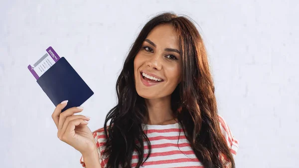 Mujer positiva sosteniendo pasaporte con billete de avión mientras mira a la cámara - foto de stock