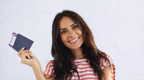 Femme joyeuse tenant passeport avec billet d'avion tout en regardant la caméra — Photo de stock