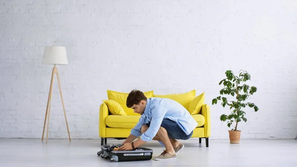 Homem de camisa azul bagagem de embalagem na sala de estar moderna — Fotografia de Stock