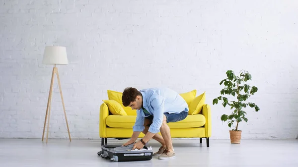 Man in blue shirt packing baggage in living room — Stock Photo