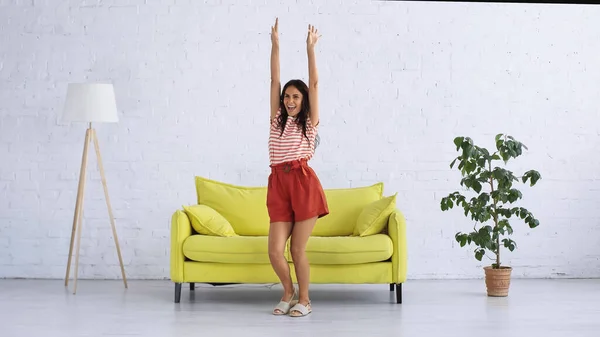 Donna felice che balla vicino al divano nel soggiorno moderno — Foto stock