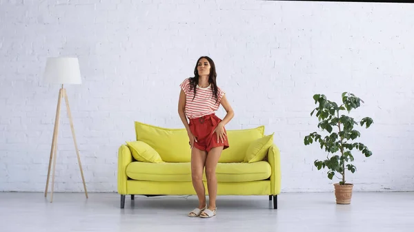 Mujer feliz bailando cerca del sofá en la sala de estar moderna - foto de stock