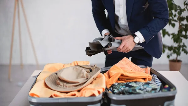 Cropped view of businessman in suit holding swim fins while packing luggage — Stock Photo