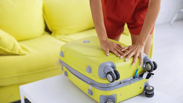 Partial view of woman leaning on yellow travel bag near sofa in living room — Stock Photo