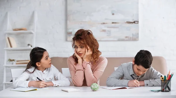 Mother sitting near kids doing homework at table — Stock Photo