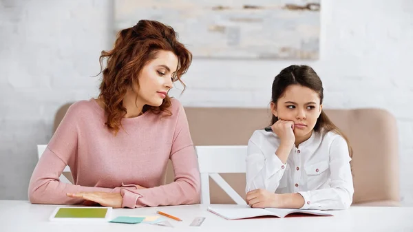 Pensive enfant tenant un stylo près du portable et de la mère pendant l'éducation à la maison — Photo de stock