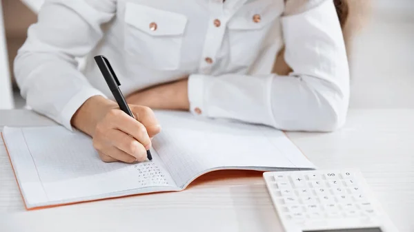 Cropped view of girl writing on notebook near calculator on blurred foreground — Stock Photo