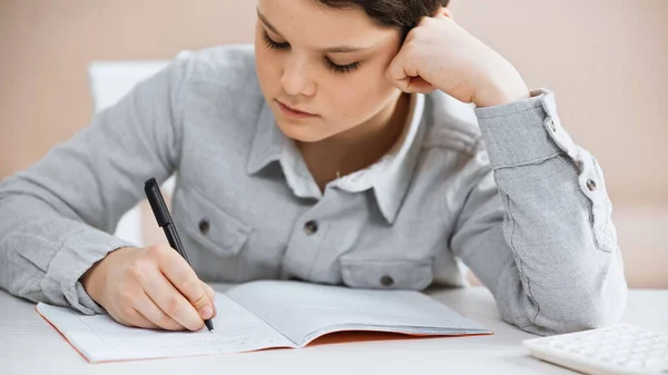 Preteen boy writing on notebook near burred calculator at home — Stock Photo