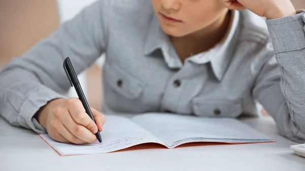 Обрізаний вид хлопчика, що пише на копіювальній книзі вдома — стокове фото