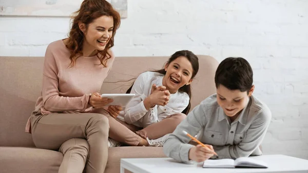 Femme positive tenant tablette numérique près de fille et fils faisant des devoirs — Photo de stock