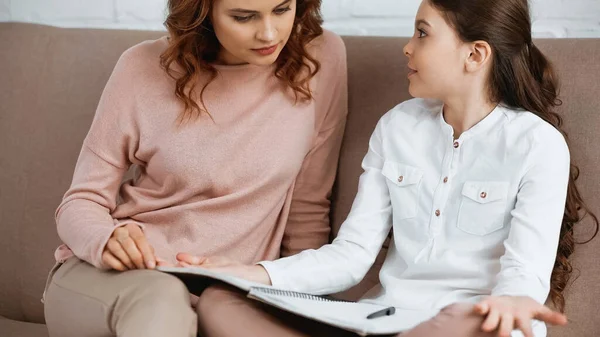 Girl with notebook looking at mother on couch — Stock Photo