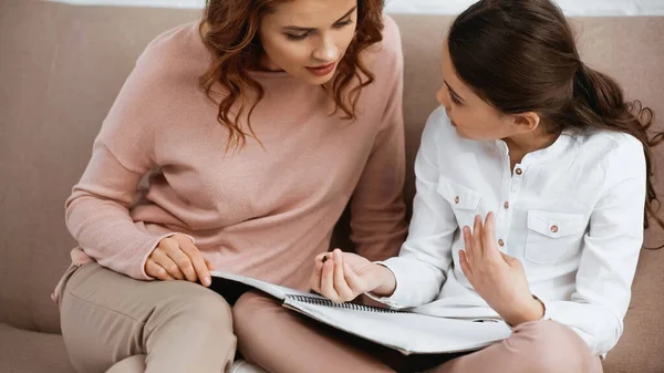 Woman helping daughter with pen and notebook during home education — Stock Photo