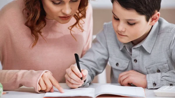 Boy writing on notebook near mother pointing with finger at home — Stock Photo