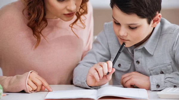 Mère assise près de l'enfant avec un stylo faisant ses devoirs — Photo de stock