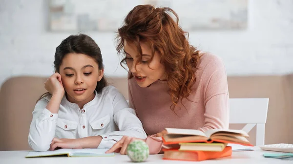 Frau spricht mit Tochter, während sie in der Nähe von Büchern bei Hausaufgaben hilft — Stockfoto