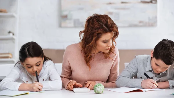 Mãe ajudando crianças com lição de casa perto da calculadora na mesa — Fotografia de Stock