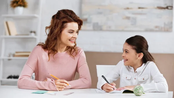 Mère et enfant joyeux faisant leurs devoirs à table — Photo de stock